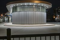 the round building is near two large poles that are at night time and lit by street lights