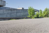 a cement structure behind some trees near a building wall and sidewalk of a parking lot