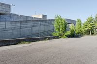 a cement structure behind some trees near a building wall and sidewalk of a parking lot