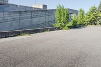 a cement structure behind some trees near a building wall and sidewalk of a parking lot