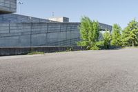 a cement structure behind some trees near a building wall and sidewalk of a parking lot