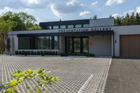 the front entrance to the presentation gallery with the building on the right side and a tree in the center