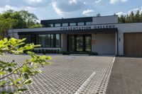 the front entrance to the presentation gallery with the building on the right side and a tree in the center