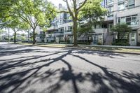 a tree lined sidewalk next to two tall buildings in a residential area surrounded by tall trees