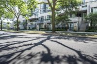 a tree lined sidewalk next to two tall buildings in a residential area surrounded by tall trees