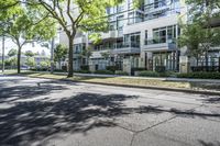 a tree lined sidewalk next to two tall buildings in a residential area surrounded by tall trees