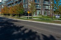 an apartment building on a street corner with trees growing in the grass beside it and a stoplight