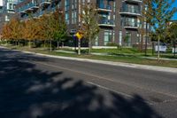 an apartment building on a street corner with trees growing in the grass beside it and a stoplight