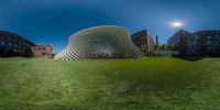 a grassy field has an enormous silver building with an oval shaped structure that appears like a dome on it