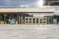 a double entrance way with wooden doors and glass walls on the building side area, while the walkway has a concrete pathway running through it