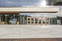 a double entrance way with wooden doors and glass walls on the building side area, while the walkway has a concrete pathway running through it