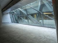 a photo inside an open space with large windows looking outside and empty flooring with white marble tile