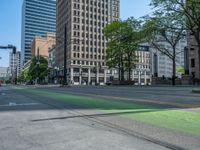 the green paint is painted on a bike path in front of an office building and large, trees