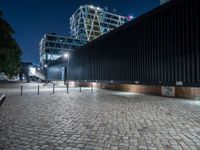 a brick walkway with lights shining down on the ground and the building at night in the distance