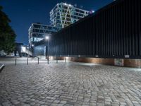 a brick walkway with lights shining down on the ground and the building at night in the distance