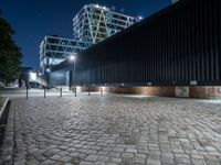 a brick walkway with lights shining down on the ground and the building at night in the distance