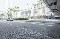 a black car driving down a road on top of bricks next to tall buildings,