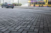 a black car driving down a road on top of bricks next to tall buildings,