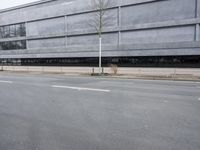 this is an empty road near a gray building with a building in the background and trees