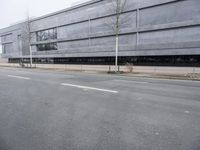 this is an empty road near a gray building with a building in the background and trees