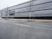 this is an empty road near a gray building with a building in the background and trees