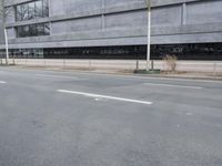 this is an empty road near a gray building with a building in the background and trees