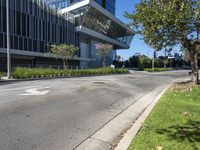 a empty road outside of a building next to a grass field and trees in the foreground