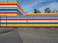 an empty parking lot painted brightly stripes on the wall of the building and sky as well as stones