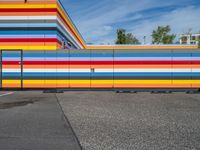 an empty parking lot painted brightly stripes on the wall of the building and sky as well as stones