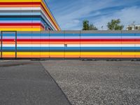 an empty parking lot painted brightly stripes on the wall of the building and sky as well as stones