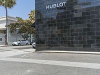 this is a street with a black building and palm trees in the background and an h ebott logo