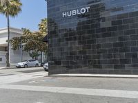 this is a street with a black building and palm trees in the background and an h ebott logo