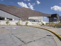 a gray building sitting on top of a parking lot next to mountains with trees near it