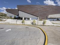 a gray building sitting on top of a parking lot next to mountains with trees near it