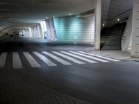 the side walk of an empty parking garage filled with parked cars and stairs, where people are walking towards a building