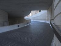 an exterior view with concrete, arched and rounded windows, and grey and white concrete flooring, and a curved building made to resemble c20