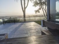 sun shining on the horizon of a balcony with a bench and trees in front of it