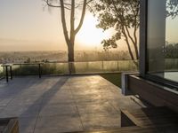 sun shining on the horizon of a balcony with a bench and trees in front of it