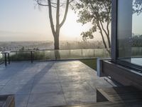 sun shining on the horizon of a balcony with a bench and trees in front of it