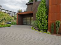 the driveway is lined with potted plants and trees, along with a paved sidewalk