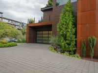 the driveway is lined with potted plants and trees, along with a paved sidewalk