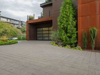 the driveway is lined with potted plants and trees, along with a paved sidewalk