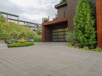 the driveway is lined with potted plants and trees, along with a paved sidewalk