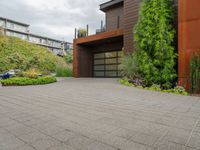 the driveway is lined with potted plants and trees, along with a paved sidewalk