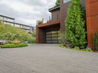 the driveway is lined with potted plants and trees, along with a paved sidewalk