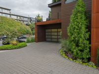 the driveway is lined with potted plants and trees, along with a paved sidewalk