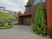 the driveway is lined with potted plants and trees, along with a paved sidewalk