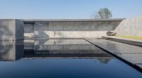 the pool is glassy and reflecting the trees in the clear water below it is a black and white bench