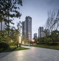 an empty park with some trees and buildings in the background at dusk, seen from across the street