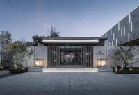 the entrance of this building is lit up at night with some lanterns and trees around it